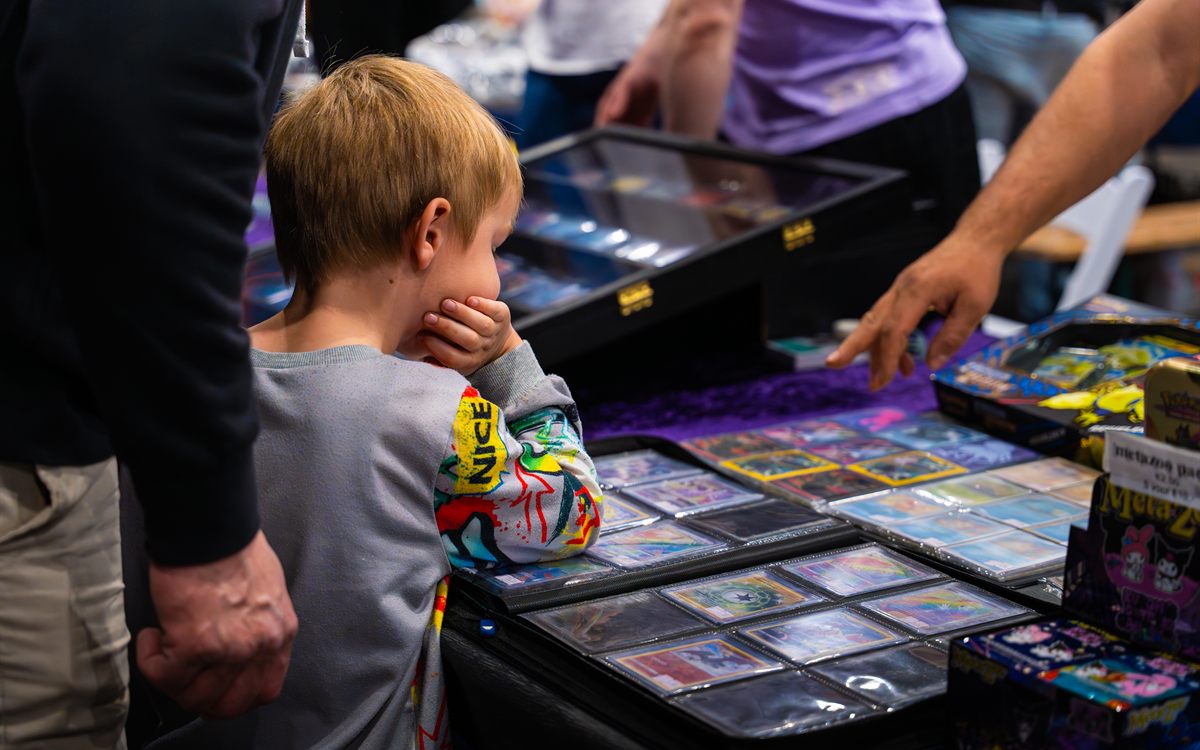 Jonge bezoeker bekijkt binders met verschillende trading cards bij een stand op Con La Posta