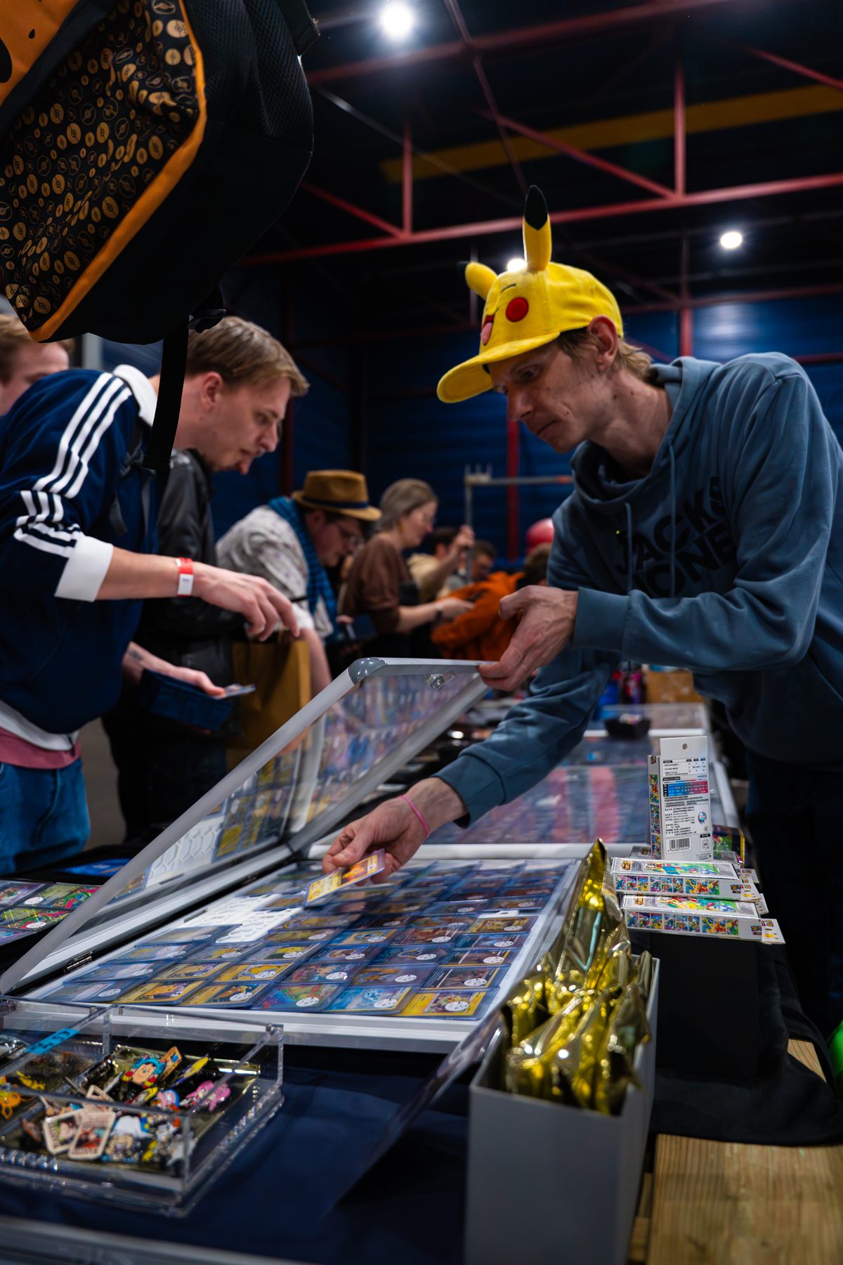 Bezoeker met Pikachu-pet bekijkt Pokémon-kaarten in een vitrine op Con La Posta