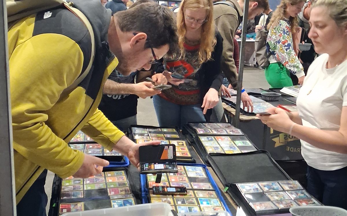 Verzamelaars vergelijken samen kaarten in binders aan de ruiltafels op Con La Posta