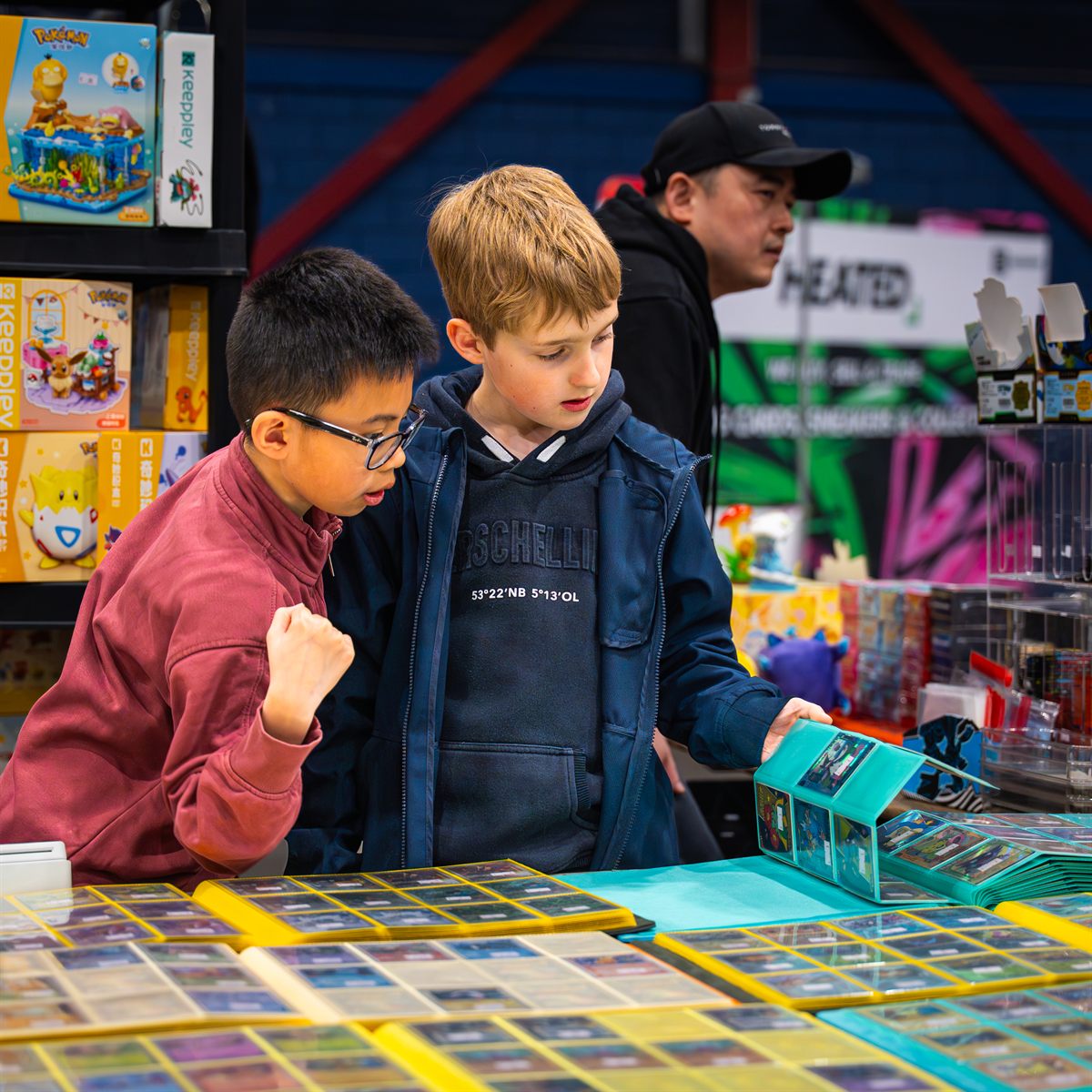 Twee jonge bezoekers bekijken samen Pokémon-kaarten in binders bij een stand op Con La Posta
