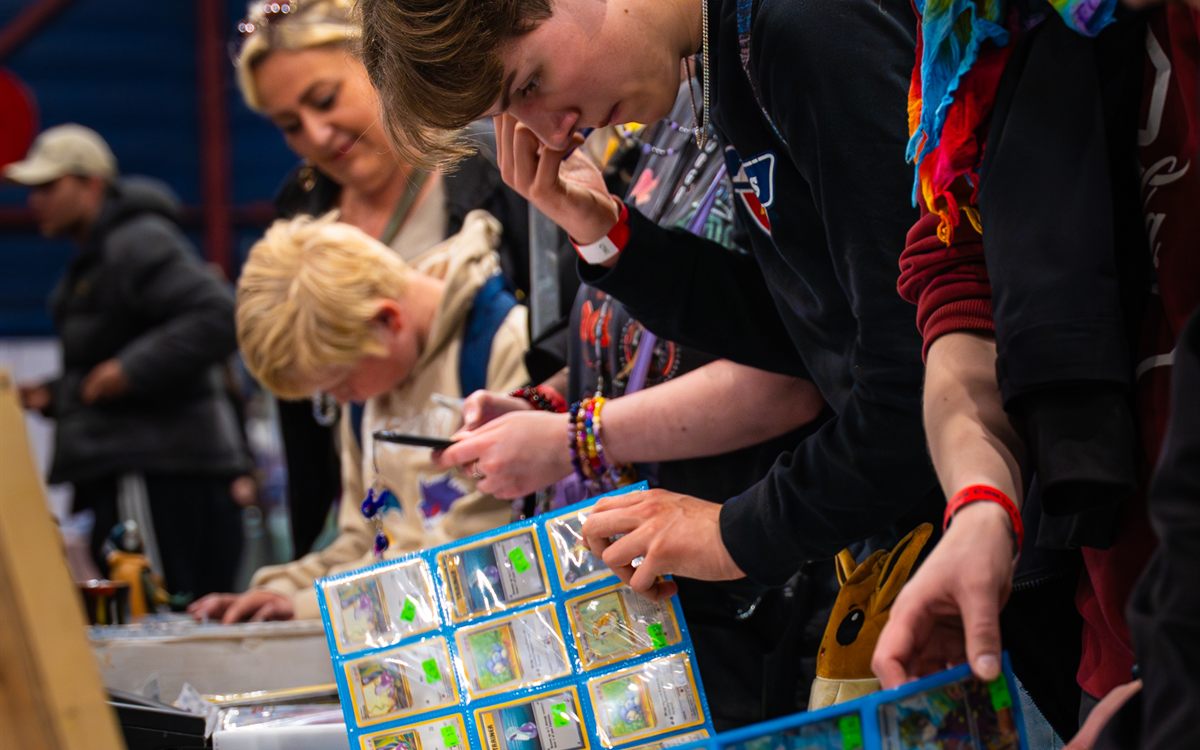 Bezoekers bekijken Pokémon-kaarten bij een vendor-tafel op Con La Posta
